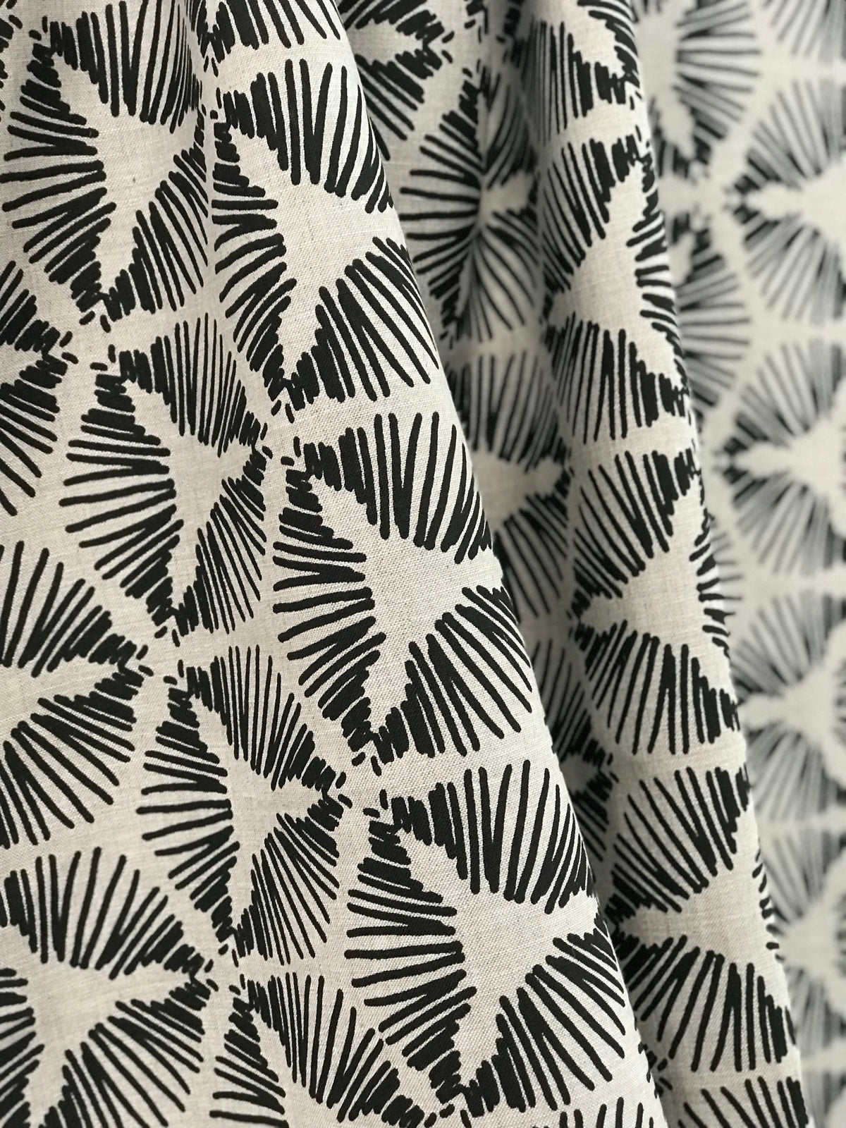 Cie by Greige Textiles — a dramatic starburst shield motif that brings graphic energy and sculptural movement to interiors. Hand printed on Belgian linen, it&#39;s a bold choice for drapery, statement cushions, or tailored upholstery.